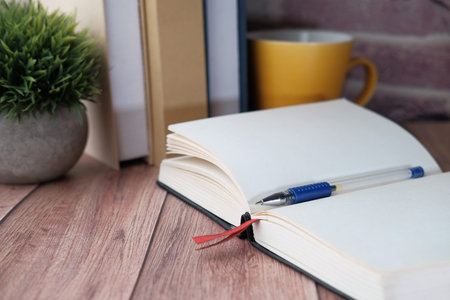 Close up of open diary, pen and books on table.