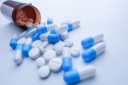 drugs and capsule spilling from container on color background