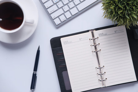 high angle view of open diary, tea and keyboard on office desk.