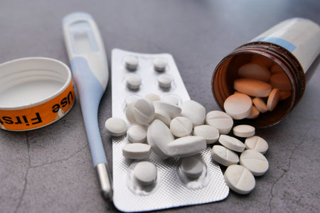 close up of pills spilling and thermometer on tableの写真素材