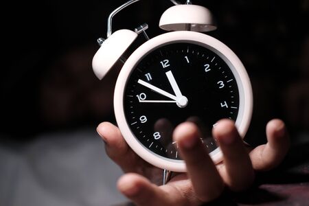Close up of hand holding alarm clock on tableの写真素材