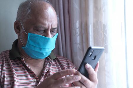 senior man with mask using smart phone indoorの写真素材