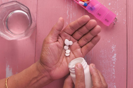 Elderly woman pouring pills from bottle on hand, top view