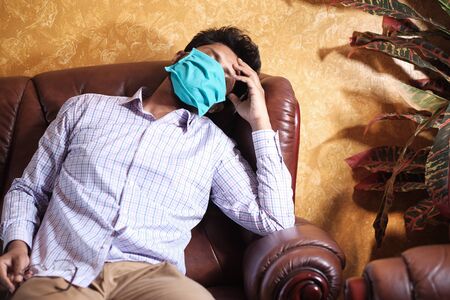 A sick man with a mask on his face resting on sofaの写真素材