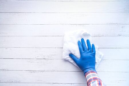 Hand in a blue rubber glove wipes on a wooden tableの写真素材