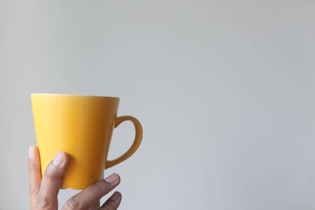 hand holding yellow mug against a wall.の写真素材