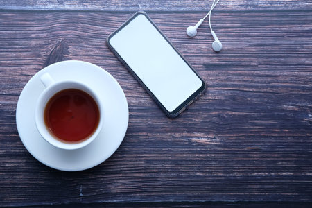 Top view of smart phone with empty screen and notepad on wooden table