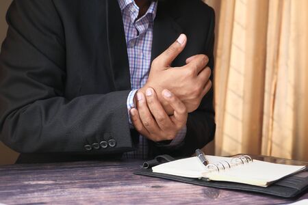 Businessman in suit pain in wrist while woking on deskの写真素材