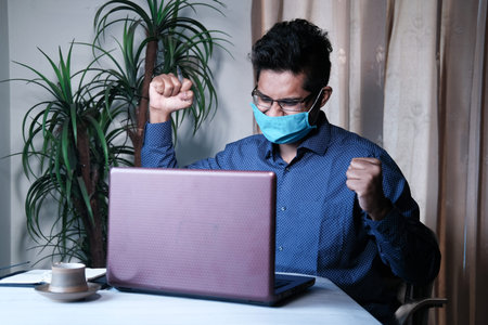 Man in face mask using laptop working from home.
