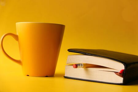 notepad with pencil and coffee mug on yellow backgroundの写真素材
