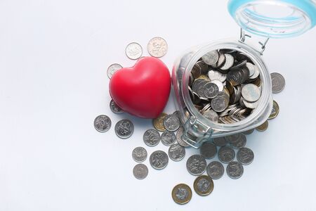 Red heart and coins in a jar on white backgroundの写真素材