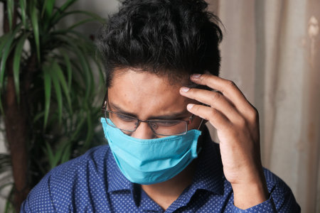 A young asian man mask on his face suffering headache