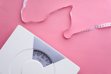a tape measure and Bathroom scale on pink background
