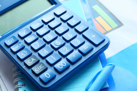Close up of blue calculator and financial chart on table.
