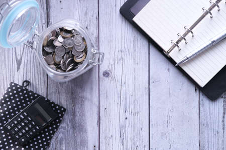 high angle view of open notepad and coins in a jar on tableの写真素材