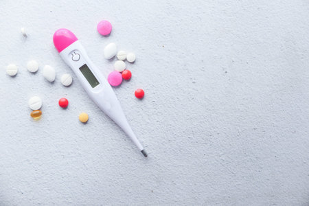 digital thermometer and pills on white texture background