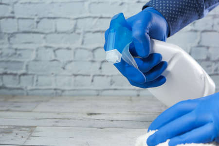 Person hand in disposable gloves using disinfectant spray to clean table surfaceの写真素材