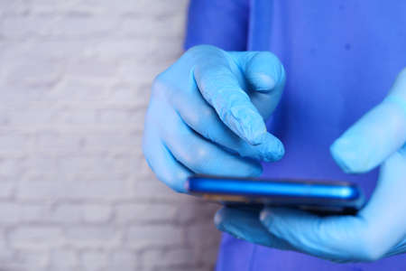 doctors hand in protective gloves using a smartphone.の写真素材