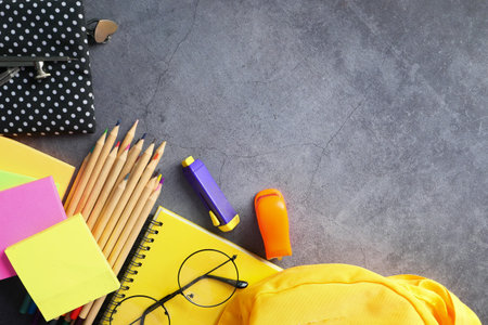 Top view of yellow backpack with different colorful stationery on table.