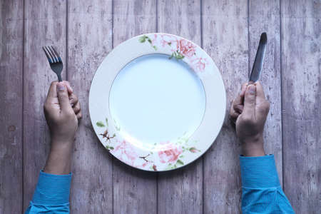 hand holding cutlery and empty plate on wooden background top downの写真素材