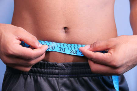 young man measuring his waist with a tape measure, close up.の写真素材