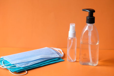 Surgical masks and hand sanitizer on orange background