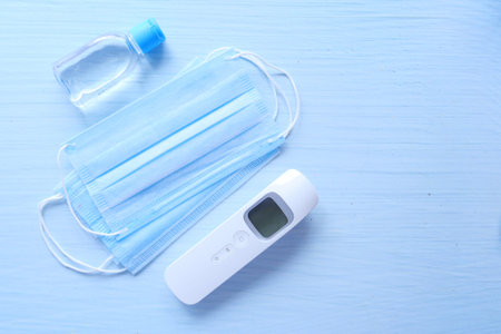 Surgical masks, thermometer and hand sanitizer on color background