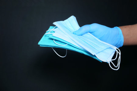 man hand holding surgical face mask isolated in black