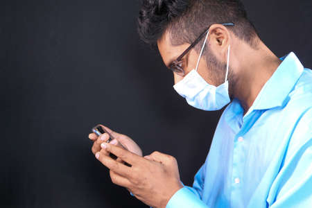 young man with face mask using smart phone indoorの写真素材