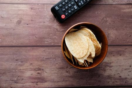 bowl of chips and tv remote on wooden background .