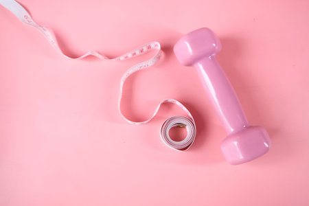 Fitness concept with dumbbell and measurement tape on pinkの写真素材