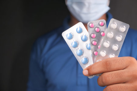 man in protective mask holding blister pack isolated in black