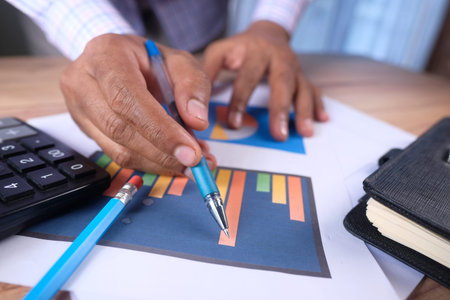 man hand with pen analyzing bar chart on paperの写真素材