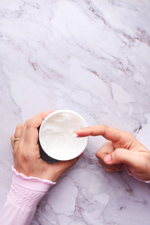 woman applying beauty cream onto skin at home top view