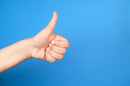 womens hand hand showing a thumb-up on blue background