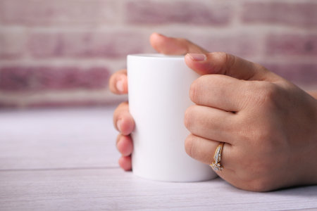 Close up of womens hand holding white color coffee cup.