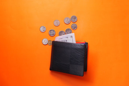 cash in wallet and coins on orange background
