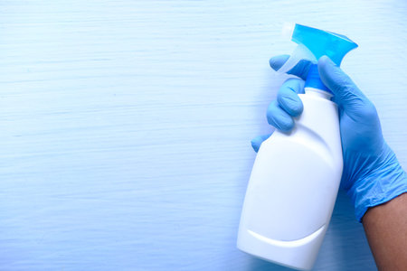 hand in blue rubber gloves holding spray bottle with copy space