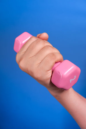 Close up of woman hand holding pink dumbbell isolated in blue