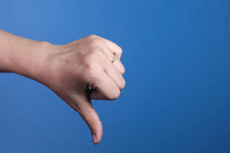 hand showing thumb down sign on blue background.の写真素材