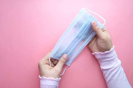 top view of women hand holding surgical face mask on pink backgroundの写真素材
