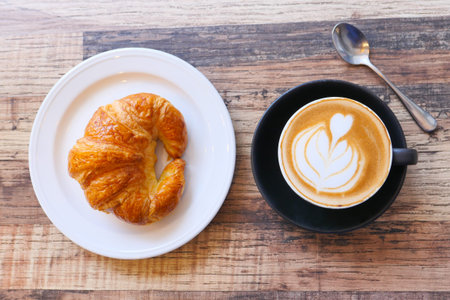 Coffee and croissant on wooden table, top view .