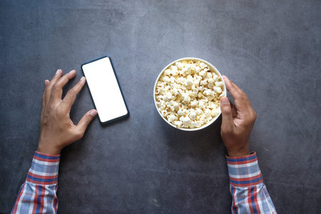 man hand using smart phone and eating popcorn