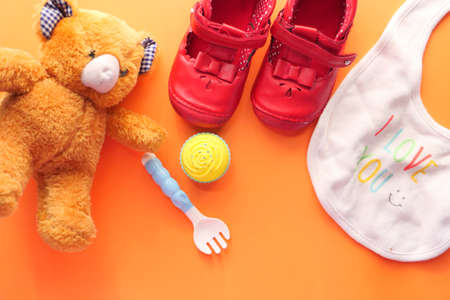 Toys for newborn baby set with teddy bear and shoe on orange backgroundの写真素材