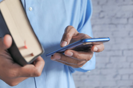 close up of man using smart phone and holding a book