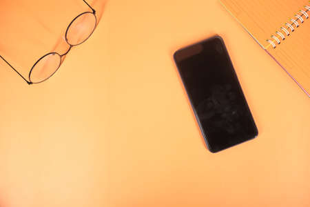 top view of smart phone and notepad on orange backgroundの写真素材