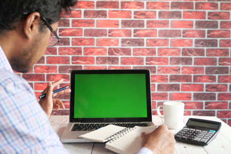 rear view of young man using laptop with blank screen on office desk.