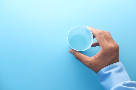 hand holding plastic glass of blue background