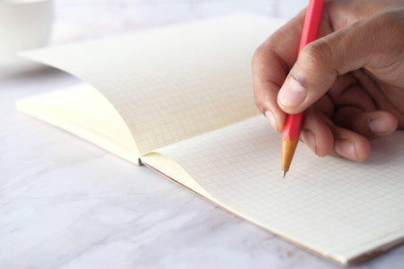 Close up of man hand writing with pencil on notepad.