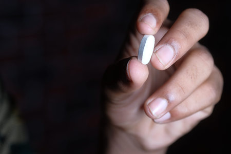 Close up of man hand holding a pill on black background